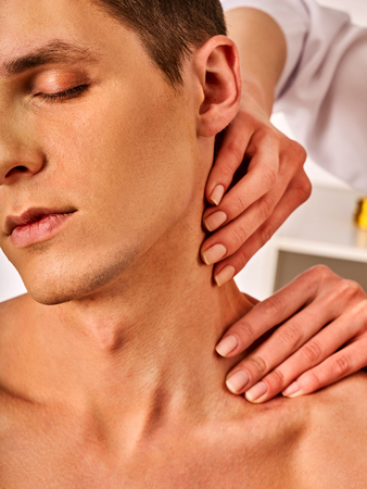 Shoulder and neck massage for man in spa salon. Doctor making therapy in rehabilitation center . Folded towels in the background. Correction of dislocation of neck by experienced specialist.の写真素材