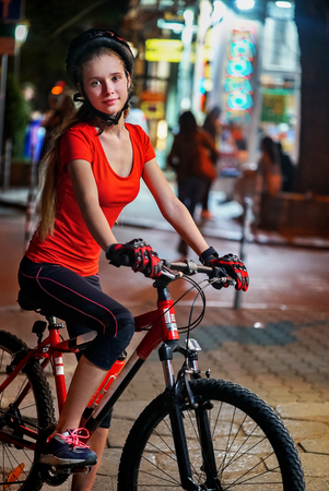 City night bicycle ride. Girls wearing bicycle helmet. Nightlife and passer people in city background.の写真素材