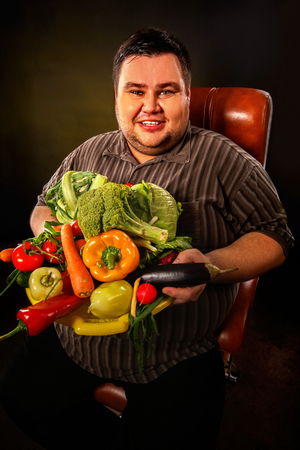 Diet fat man eating healthy food with vegetables cauliflower and sweet pepper with radish, tomatoes for overweight person. Fat man with a hill of fresh vegetables. Abundance of food concept.の写真素材