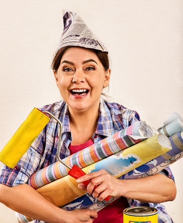 Repair home elderly woman holding paint roller for wallpaper. Happy senior woman in newspaper cap renovation apartment and calling for help .の写真素材