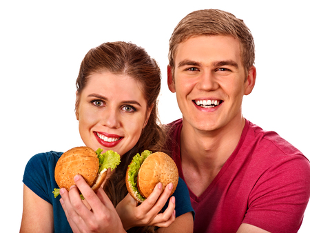 Couple eating fast food. Man and woman eat hamburger with ham. Friends holding two burder junk on white background isolated. People try feed each other. Use of semi-finished products is undesirable.の写真素材