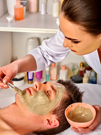 Mud facial mask of woman in spa salon. Massage with clay full face. Girl on with therapy room. Healing clay to preserve youth. Beautician with bowl therapeutic procedure isolated background.の写真素材