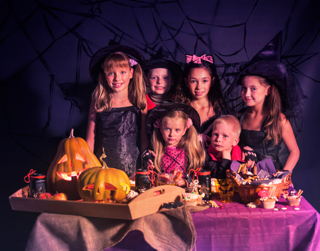 Halloween kids prepering carved pumpkin as jack-o-lantern with trick or treat food at table. Black background.の写真素材