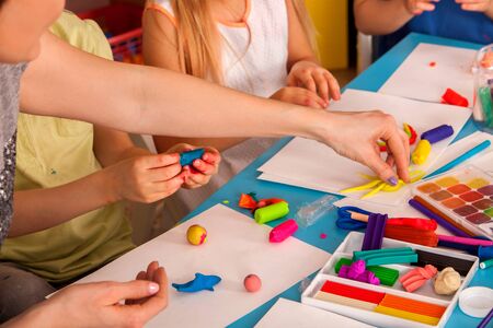 Plasticine modeling clay in children class. Teacher teaches kids together play dough and mold from plasticine in kindergarten or preschool. Group of four people. They learn to live in a team.の写真素材