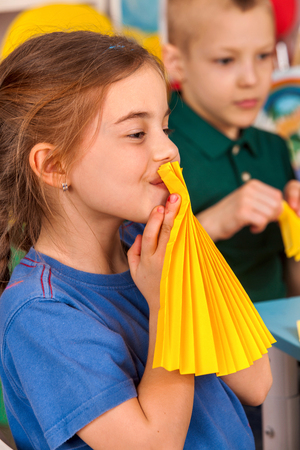 School children with paper in kids hands in class room. Development and social lerning. Childrens project in kindergarten. Girls and boy together. . Team makes paper fans.の写真素材