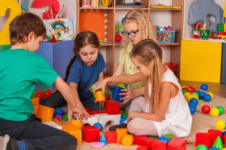 Children building blocks in kindergarten. Group kids playing toy on floor. Top view of interior preschool. Building a tower of cubes. Newcomer in childrens team.の写真素材