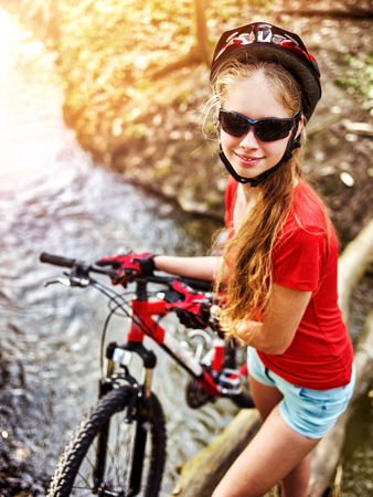 Cycling teen with ladies bikes in summer park. Woman road bike for running on nature. Teenager girl in helmet bicycle fording throught water. School trip. Sun flare background illumination.の写真素材