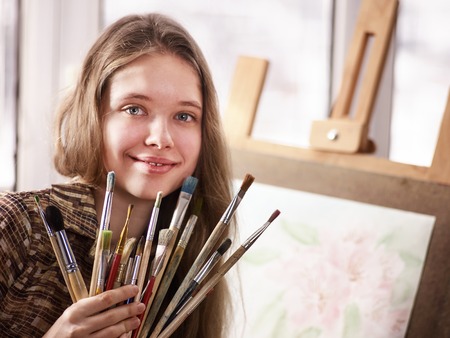 Artist painting on easel and palette in studio. Authentic girl paints with oil brush in morning sunlight . Workshop of a professional artist. Student prepared gift for her teacher.の写真素材