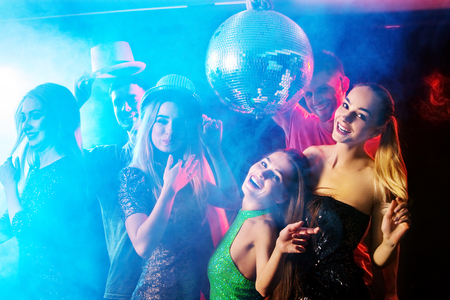 Dance party with group people dancing. Women and men have fun in night club. Back light on girls...