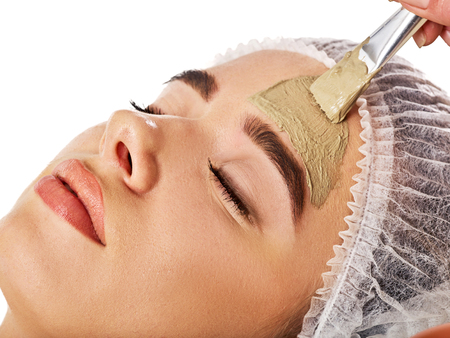 Mud facial mask of woman in spa salon. Massage with clay full face. Girl on with therapy room. Beautician with brush therapeutic procedure isolated background. Healing clay for face. Facelift.の写真素材