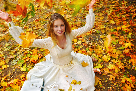 Autumn fashion feminity lace dress with long sleeve in princess style. Top view of girl model trew foliage bouquet sitting on fall leaves in city park outdoor.の写真素材