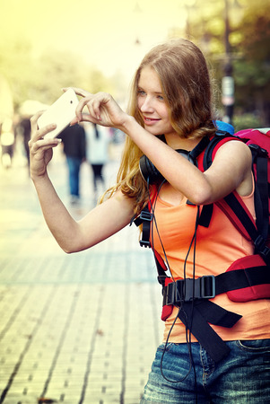 Tourist girl with backpack taking selfies on smartphone and cultural city showplace pedestrianized street outdoor. Tone image sepia.の写真素材