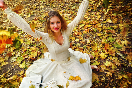 Autumn fashion feminity lace dress with long sleeve in princess style. Top view of girl model hand up with foliage bouquet sitting on fall leaves in city park outdoor.の写真素材