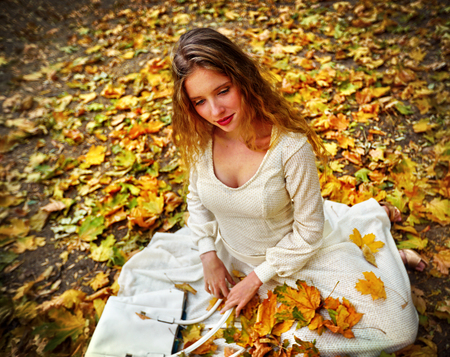 Autumn fashion feminity lace dress with long sleeve in princess style. Top view of girl model trew foliage bouquet sitting gracefully and flirt see on fall leaves in city park outdoor.の写真素材