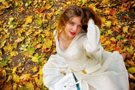 Autumn fashion feminity lace dress with long sleeve in princess style. Top view of girl model foliage yellow bouquet sitting on fall leaves in city park outdoor.の写真素材