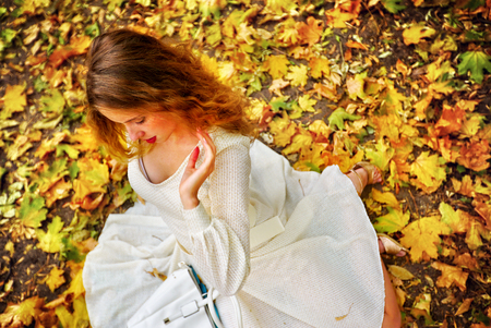 Autumn fashion feminity lace dress with long sleeve in princess style. Top view of girl model see down foliage bouquet sitting on fall leaves in city park outdoor.の写真素材