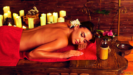 Massage of woman in spa salon. Girl on candles background in massage spa salon. Luxary interior in oriental therapy salon. dry flowers in wooden vases. Spot light on dark background.の写真素材