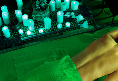 Massage of woman in spa salon. Girl on candles background in massage spa salon. Luxary interior in oriental therapy salon. Female have relax after sport. Green color tone on shiny sunlight background.の写真素材