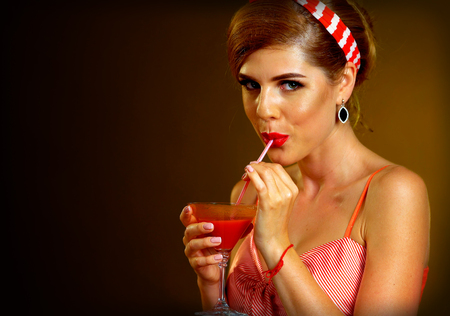 Retro woman with music vinyl record. Pin up girl drink drink through straw martini cocktail. Girl pin-up retro style wearing red dress on dark background. Illegal alcohol at party.の写真素材