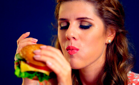 Woman eat hamburger fast food with close eyes.の写真素材
