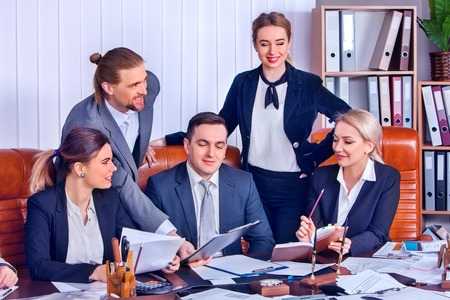 Business people office life of team people working with papers sitting table. Cabinets with folders and jalousie, flowers in pots background. Firm increased its revenues for year.の写真素材