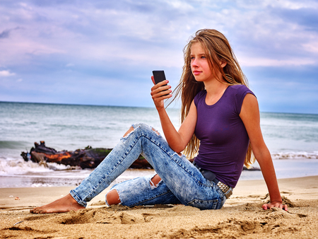 Teenager girl sitting on sand near sea call help by phone. Summer girl sea back on water. Nature beauty.の写真素材