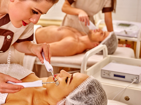 Young family receiving electric galvanic face spa massage procedure  at beauty salon. Anti-agin massage.の写真素材