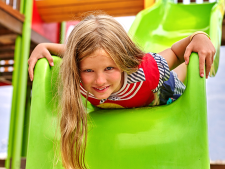 Child girl upside down on  park playground game. Girl slides on childrens slide.の写真素材
