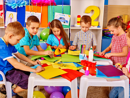 Group kids holding colored paper on table in kindergarten. Kids learning do origami.の写真素材