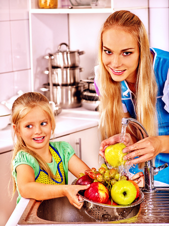 Mother and daughter washing fruit under pouring water at kitchen.の写真素材