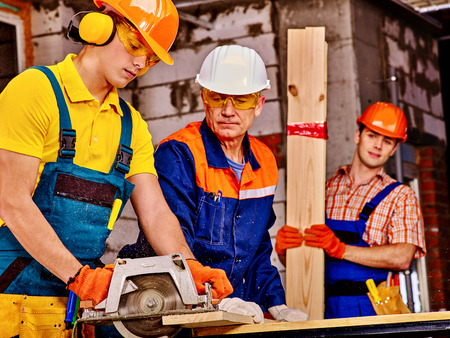 Happy group people  of three people builder with circular saw.