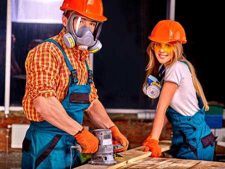 Man in gas mask and woman in builder helmet with electric planer.の写真素材
