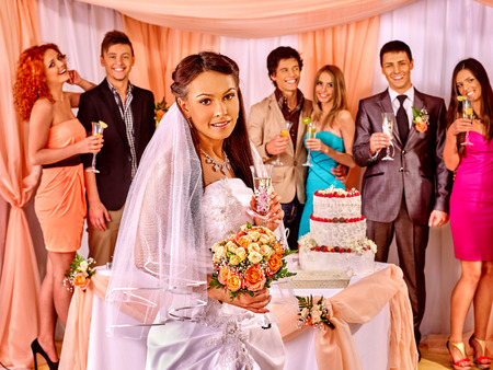 Group people at wedding table with cake. Bride with a bouquet of flowers in the foregroundの写真素材