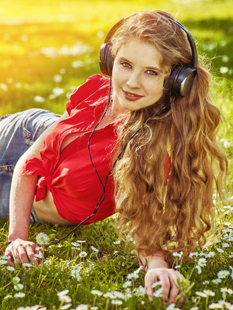 Girl in headphones catch rhythm music on green grass with chamomile flowers summer stream light outdoor.の写真素材