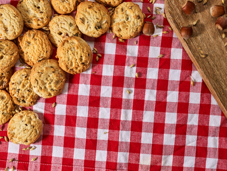 Oatmeal cookies with husk unpeeled oats and nut on kitchen cutting board gingham checkered cotton fabric on table in village style copy space with triangle for picnic.の写真素材