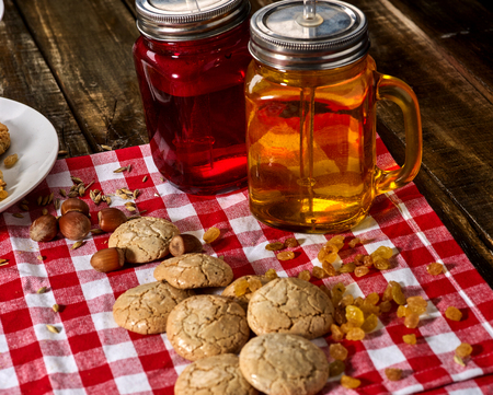 Oatmeal cookies with husk whole oats and glass mug with drinking straw on red kitchen gingham checkered cotton fabric on wooden table in farm style.の写真素材