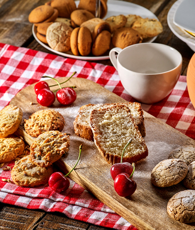 Oatmeal cookies and cherry on kitchen cutting board gingham checkered cotton fabric on table in village style for picnic with plate of macaron background. New dishes in expensive cafe Culinary coursesの写真素材