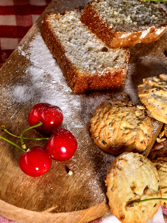 Oatmeal cookies with husk oats and cherry on kitchen cutting board gingham checkered cotton fabric on table. Fragrant Homemade Cupcake on Baking Board. Beautiful, bright sweet cherry.の写真素材