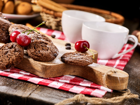 Oatmeal chocolate cookies with coffee grains and cherry, powdered sugar on kitchen cutting board with checkered fabric on wooden table in village style for picnic. Several recipes for baking.の写真素材