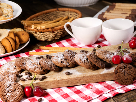 Oatmeal chocolate cookies with coffee grains and cherry, powdered sugar on kitchen cutting board with checkered fabric on wooden table in village style for picnic. Problems with excess weight.の写真素材