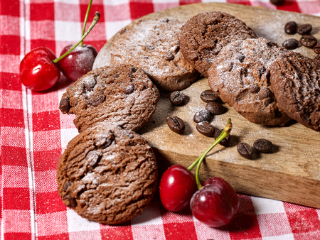 Oatmeal chocolate cookies with coffee grains and cherry, powdered sugar on kitchen cutting board with checkered fabric on wooden table in village style for picnic. Limitations for diabetics.の写真素材