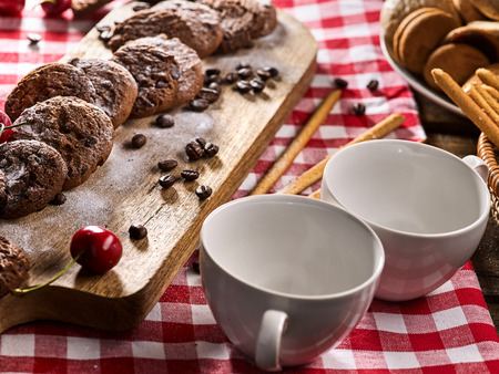 Oatmeal chocolate cookies with coffee grains and cherry, powdered sugar on kitchen cutting board with checkered fabric on wooden table in village style for picnic. Proper nutrition.の写真素材