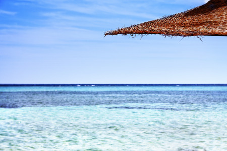 Beach on crystal with azure ocean with straw umbrella with horizon background.の写真素材