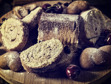 Rolled biscuit and sand chocolate cookies on board. Cinnamon stick and cherry on kitchen wood table tone image in rustic style.の写真素材
