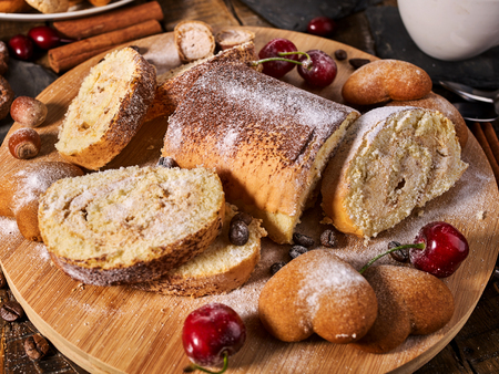 Rolled biscuit and sand chocolate cookies on board. Cinnamon stick and cherry on kitchen wood table in rustic style. Cherry in powdered sugar.の写真素材