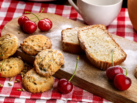 Oatmeal cookies and cherry on kitchen cutting board gingham checkered cotton fabric on table in village style for picnic. Best selection of sweets. Beautiful, expensive, culinary masterpieces.の写真素材
