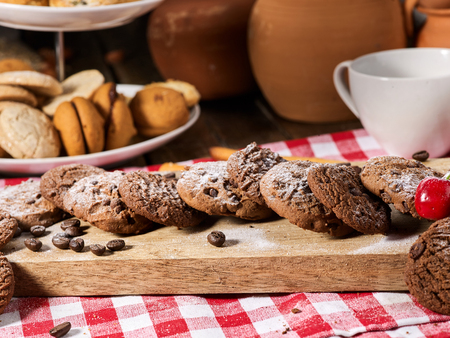 Oatmeal chocolate cookies with coffee grains and cherry, powdered sugar on kitchen cutting board with checkered fabric in village style for picnic. Easily digestible and quickly digestible substances.の写真素材