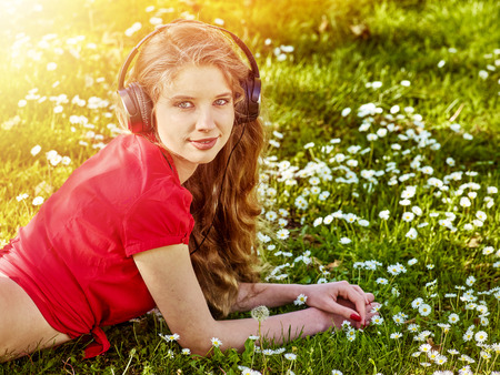 Girl in headphones catch rhythm music on green grass with chamomile flowers summer outdoor. Sunny sunset on beautiful meadow.の写真素材