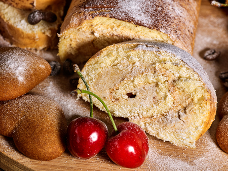 Sand chocolate cookies heart shape and rolled cake with cherry and cinnamon stick on kitchen on wooden table in village style morning sun flare. Freshens usual recipe.の写真素材