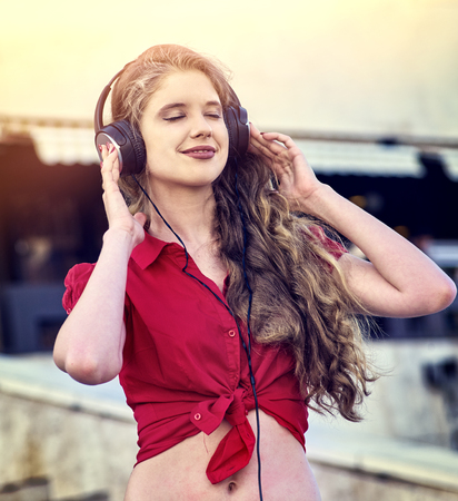 Girl in headphones listens to music in city. Color tone on shiny sunlight background.の写真素材